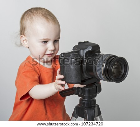 young child playing with digital SLR camera. Neutral grey background