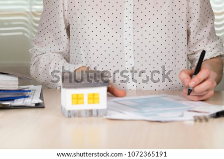 Young woman makes some calculations. Small paper house in the background