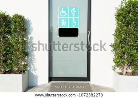 Close up toilet door with sign of disabled people, elderly, pregnant woman, and baby for their with welcome doormat and plant by the side.