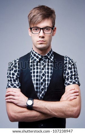 Portrait of young stylish man in glasses and with wristwatch on a gray background