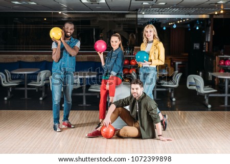 happy young friends posing with balls at bowling club
