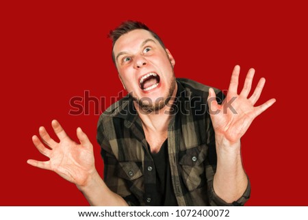 Young crazy guy scares like a devil with hands up  on red background.