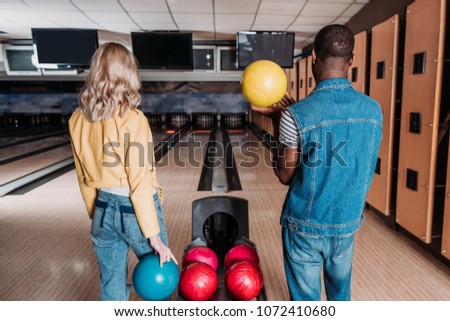 multiethnic couple with bowling balls standing in front of alleys at club
