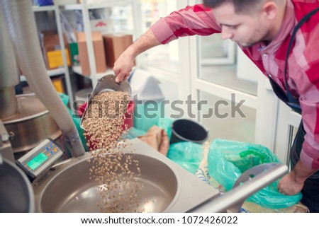Image of man with scoop with coffee beans at coffee grinder