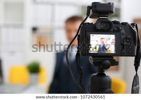 Male in suit and tie show confirm sign arm making promo videoblog or photo session in office camcorder to tripod closeup. Vlogger promotion selfie solution or finance advisor management information