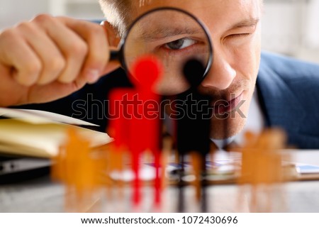 Man in suit look thru loupe on statuettes closeup in office. Success hr assessment people headhunt inspector applicant exchange concept Royalty-Free Stock Photo #1072430696