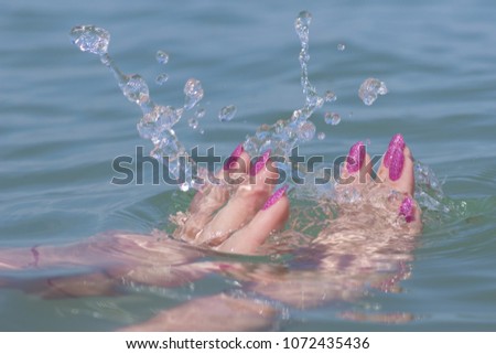 Female hands with pink nails in sea water and splashes