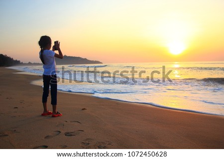 Little girl taking photos on the beach Kid girl on the beach with phone taking photos of a seascape view. child is making selfie on a sunset ,Thailand 