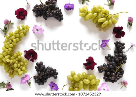 Frame of black and green grapes, lilac flowers on a white background. The pattern of grapes of different varieties, top view. Food background.
