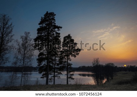 Beautiful nature and landscape photo of colorful sunset at spring evening in Sweden Scandinavia Europe. Nice outdoors image with lake, trees and sky. Calm, peaceful background picture.