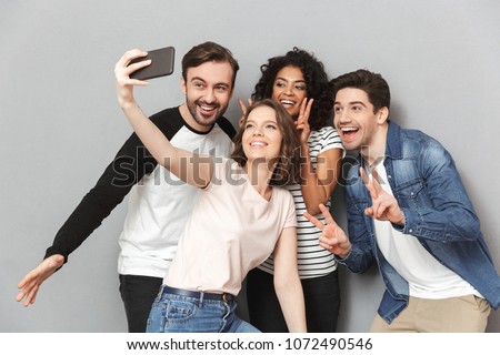 Photo of happy group of friends standing isolated over grey wall background looking aside make a selfie. Royalty-Free Stock Photo #1072490546