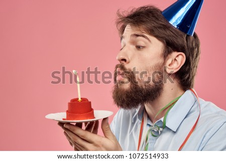  a man in a blue cap blows out a candle on a red cake                              