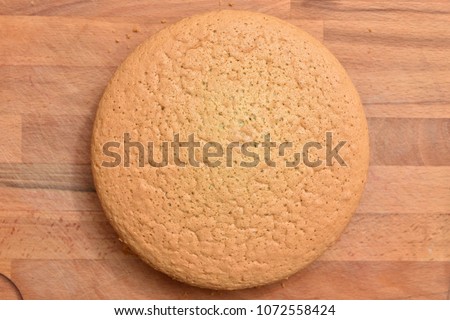 Fresh baked, round cake is on a wooden surface, the texture is visible