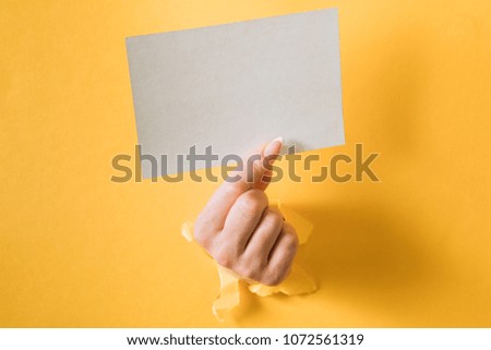 Hands with a business card punching a hole in a yellow background