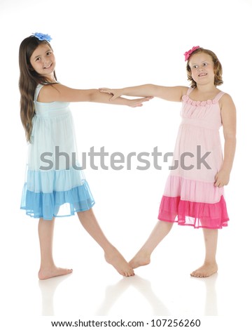 Two happy elementary girls dancing in identical dresses except one is blue, the other pink.  On a white background.