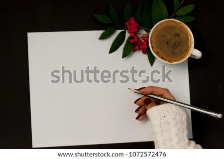 a cup of coffee rowan or a shoal on a black background and the hand writes on the sheet an empty space for the text