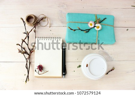 Copy book with empty shirt, cup of coffee, gift box wrapped with blue cloth, branch of spring tree with cute buds, dry flower of pink rose. Objects on wooden background, overhead view