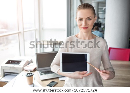 A picture of happy and cheerful woman having laptop in her hands. She has a pen in her left hand and show with it to the tablet's screen.