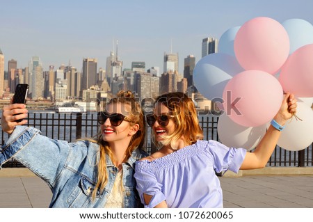 Beautiful young women taking a selfie with her smartphone on New York view. Fashionable girls with balloons, summer travel in USA
