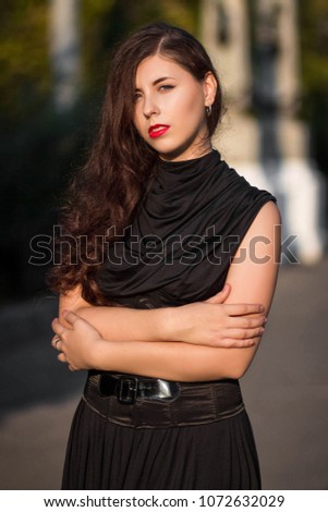 Young, beautiful girl in a black dress with a corset, on a park background and stone columns with lanterns.
