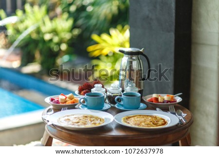 Traditional balinesse breakfast with two blue cups of hot drink on wooden table