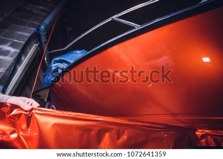 Car wrapping specialist putting vinyl foil or film on car. cutting protective film with torch. wrapping yacht, boat, ship, car, mobile home. orange film
