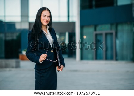 Smiling businesswoman poses against business center. Modern financial building, cityscape. Successful female businessperson