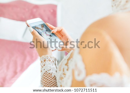 The bride looks at the phone with her photo in a bright room