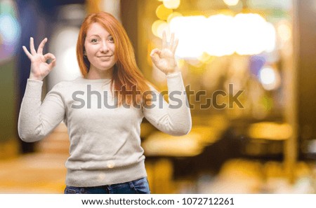 Beautiful young redhead woman doing ok sign gesture with both hands expressing meditation and relaxation at night