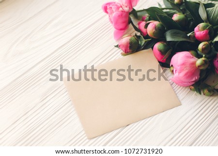 lovely pink peonies with empty craft card on rustic white wooden background top view, space for text. floral greeting card mock-up. beautiful flowers. happy mothers day concept