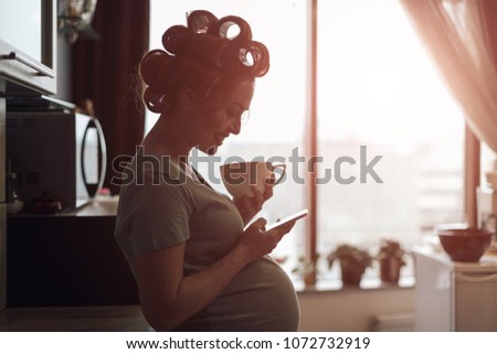 Pregnant woman got good news. Female profile picture while drinking a cup of tea while using smartphone, near the window with city reflection in it. Female silhouette profile picture.
