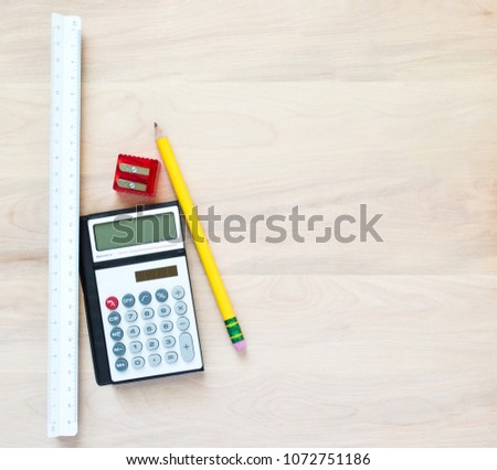 a yellow pencil, a red pencil sharpener, a small calculator and a triangular ruler on a wooden desk with copy space