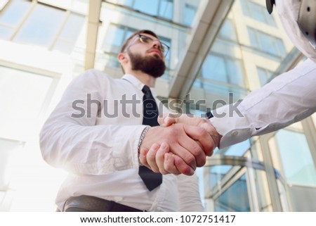 Handshake of two young men against a multi-storey office building. Make a deal. Friendly relations. Office staff. Signing of the contract.