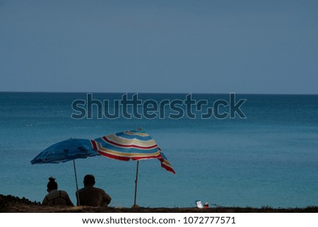 People is sitting beneath colorful sea umbrella with deep blue sea in background, Thailand