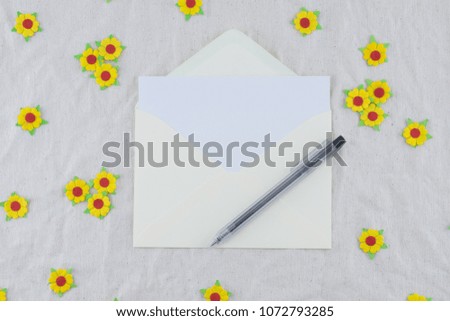 White card in yellow envelop with black pen decorate with yellow paper flowers on muslin fabric