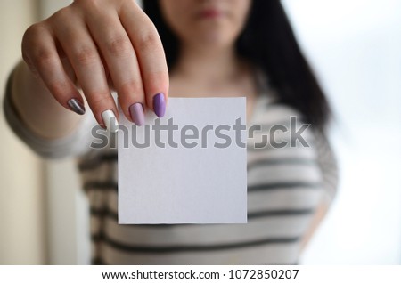 Young sad girl shows a white sticker. Caucasian brunette holding a blank sheet of paper as a template for your text