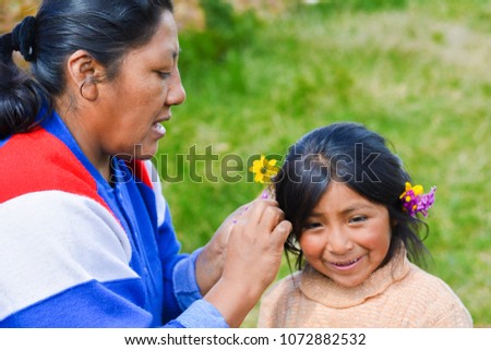 Native american mom decorating hair of her little daughter with flowers.