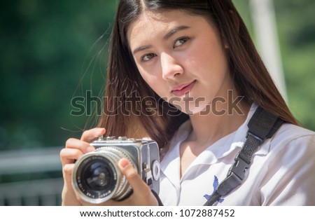Millennials using analog technology: young Thai girl taking pictures with a vintage medium size film camera outdoors