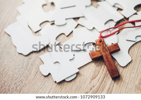 close up of Wooden cross over jigsaws on wooden table against window light, christian concept show Jesus is most important part which fulfill in human life, copy space
