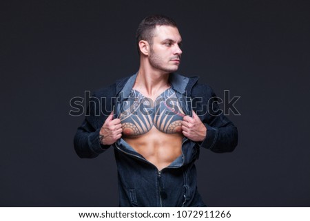 The man with a muscular torso with tattoos on the dark background