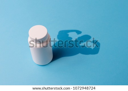 Plastic Bottle with Tablets and the Shadow with the Hands of the Bodybuilder. Concept of Steroids and Pharmaceutical Preparations for Bodybuilders. Pharmaceutical Preparations for rapid muscle growth. Royalty-Free Stock Photo #1072948724