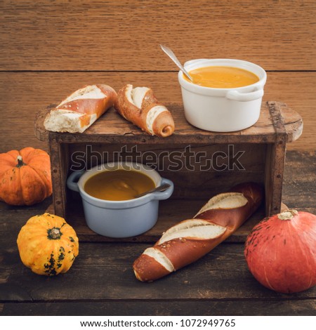 Homemade pumpkin soup in little cocotte cups and pretzel sticks on wooden table