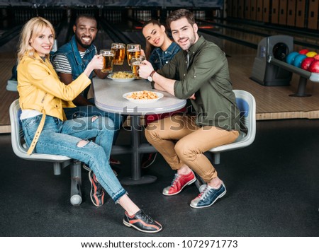 group of friends clinking mugs of beer at bowling club in front of alleys