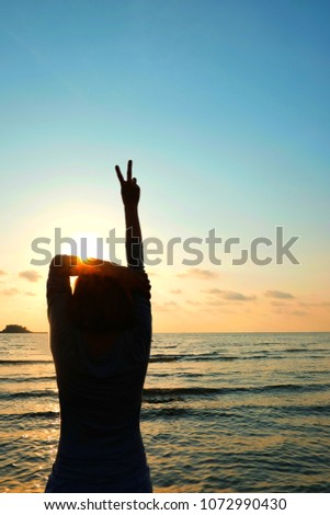 Women raised their arms and held two fingers to mark the fight. The sun is going to be the background. Silhouette image.
