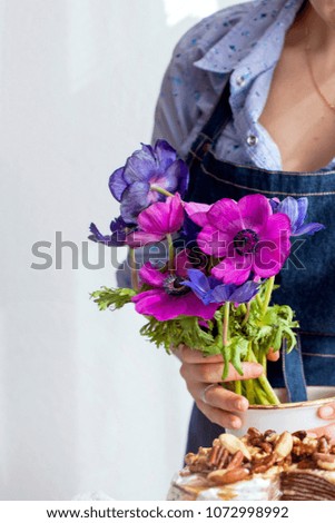 A girl in an apron holds a bouquet of flowers of blue and pink in her hands. Good Morning at home. Place for text
