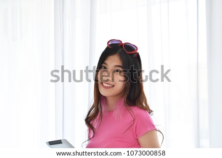 Portrait beautiful Asian girl standing and play tablet near window with white Curtain, look at camera.