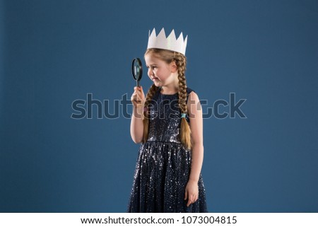 Happy girl in princess costume looking through magnifying glass