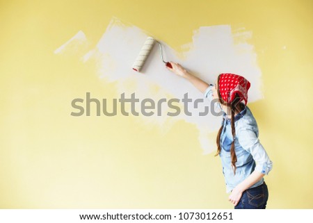 Beautiful girl in red Headband painting the wall with paint roller. Portrait of a young beautiful woman painting wall in her new apartment Royalty-Free Stock Photo #1073012651