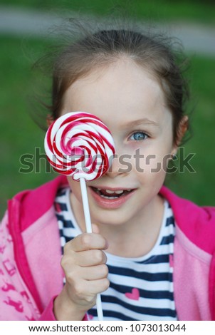 Adorable little Caucasian Girl Holding Lollipop or Sweet Candy Happy Expressions. Standing over Blured Green Grass Background