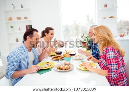 Side view portrait of cheerful, beautiful women and handsome stylish men gathering in house, apartment, room, festive company sitting at the table discussing, talking, enjoying, having fun, laughing